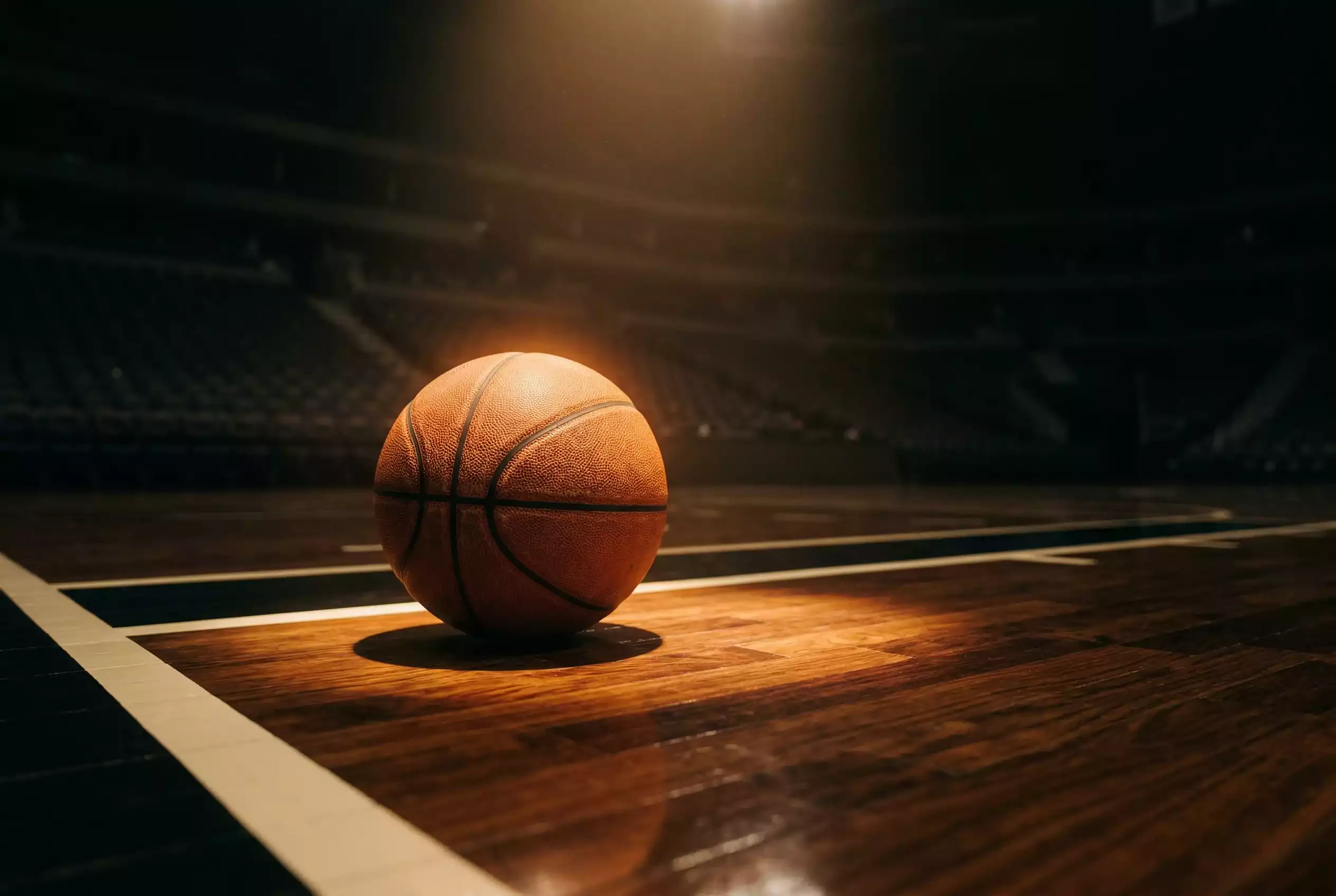 Basketball Wetten: orangefarbener Basketball auf einem Hallenparkett im Scheinwerferlicht